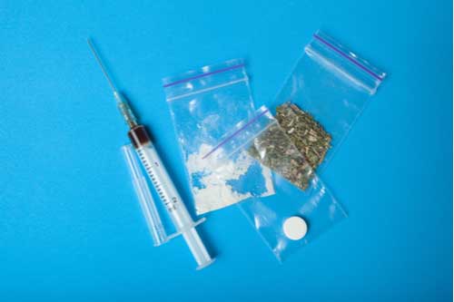 Drug needle and bags with marijuana, cocaine, and a pill