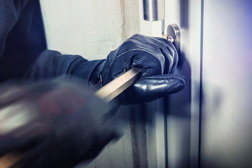 A burglar forcing open a door, concept of theft defense attorney