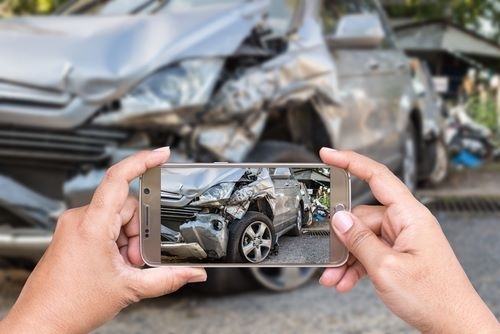 A driver taking pictures of a damaged car after a crash
